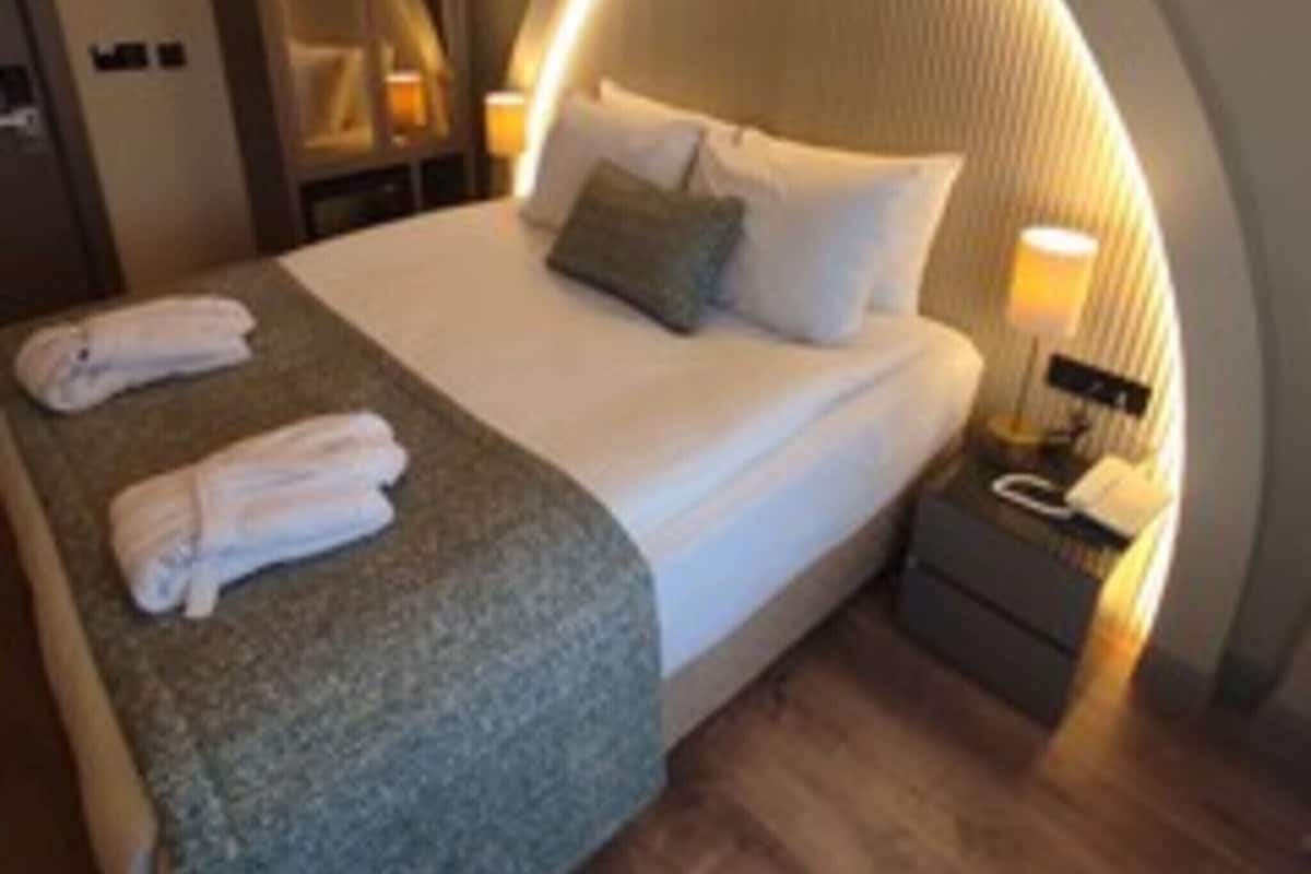 A hotel room with a bed, bedside tables, a mirror, and a lamp.