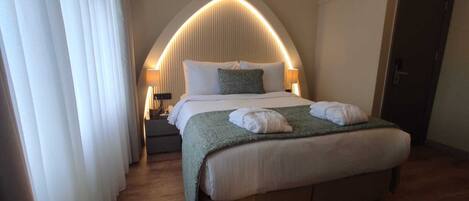 A hotel room with a large bed, a curved wall design, an air conditioning unit, and a door.