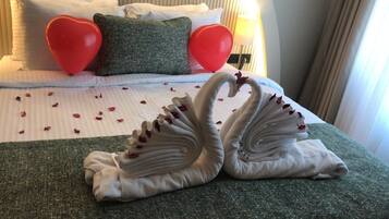 Una cama con almohadas con forma de corazón, una toalla dispuesta en forma de cisne y pétalos de rosa esparcidos sobre la cama.