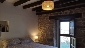 Ein Schlafzimmer mit einem Bett, einer Nachttischlampe, einer Pendelleuchte, einer Steinwand und einem Fenster.