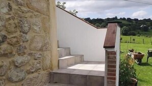 Stufen aus Stein und Ziegel führen zu einer weißen Tür, im Hintergrund ein Garten und Hügel.