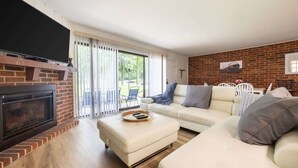 A living room with a fireplace, a sofa, a TV, and a sliding glass door to the outside. - Charming 1BR Condo with Patio, Near The Lake Geneva (Lake Geneva)