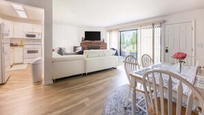 A modern living room with a white sofa, a dining table with chairs, a fireplace, and a kitchen area with white cabinets and appliances. - Charming 1BR Condo with Patio, Near The Lake Geneva (Lake Geneva)