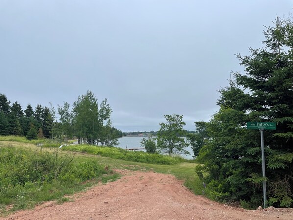 Un sentier de terre mène à un plan d’eau, entouré d’arbres, et un panneau indique « Allée Patty’s Ln ».