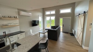 Et rummeligt køkken med en stor ø, et spiseområde med et bord og stole, en grå sofa og en skydedør i lade-stil.