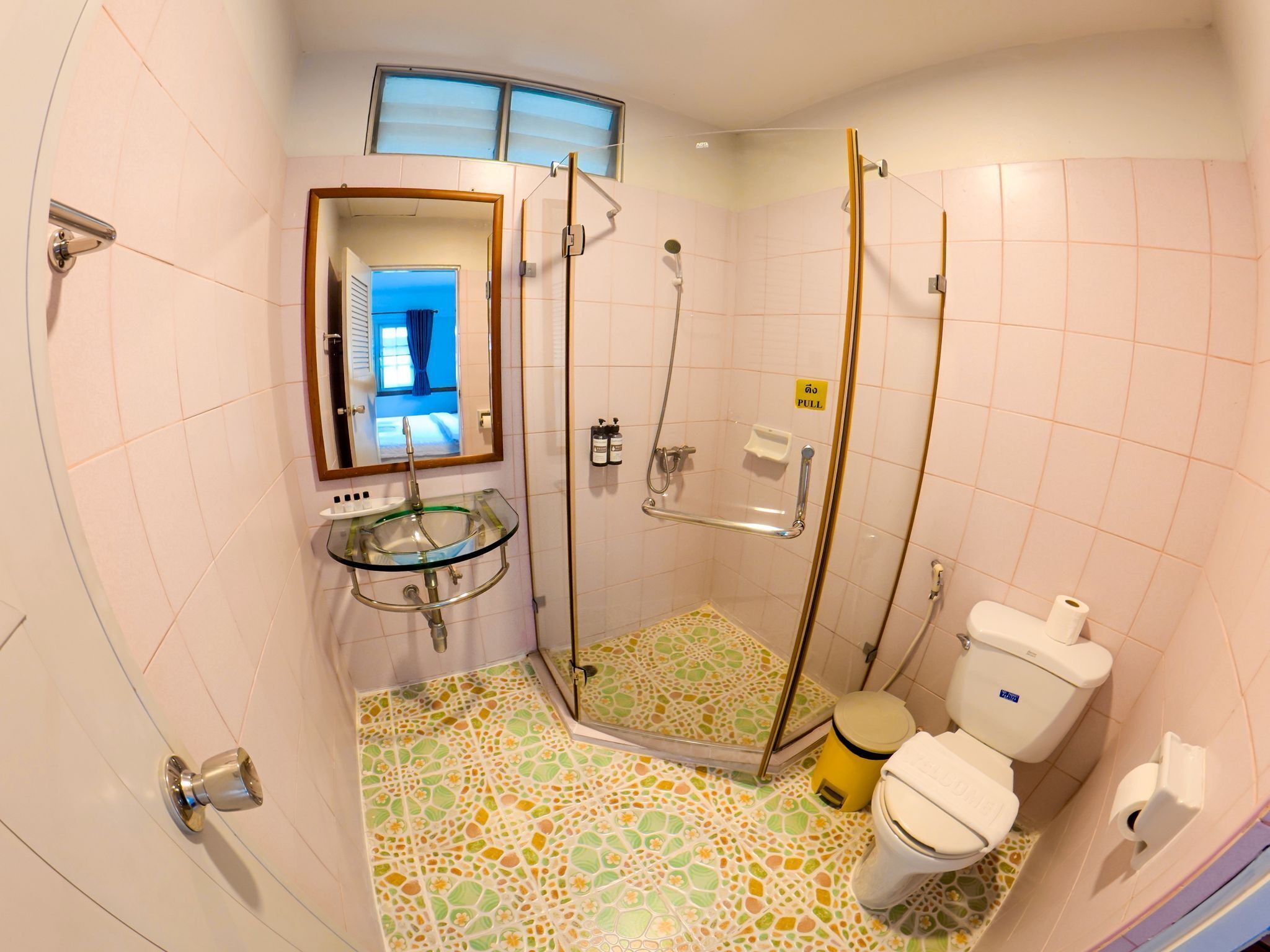 A bathroom with a glass sink, a shower with a pull handle, a toilet, and a patterned floor.