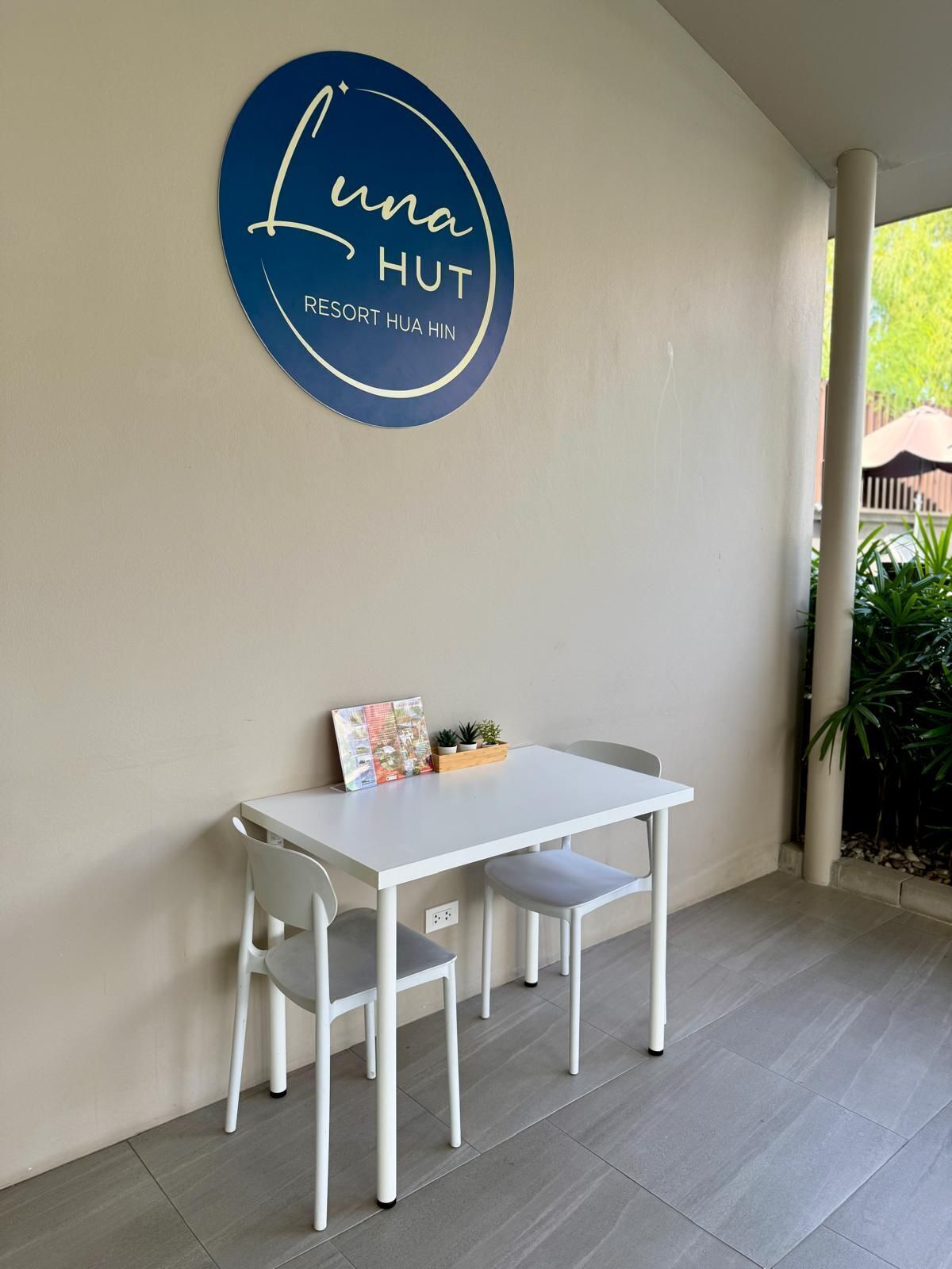 Schild des Luna Hut Resorts, ein weißer Tisch mit zwei Stühlen und eine kleine Pflanze darauf.