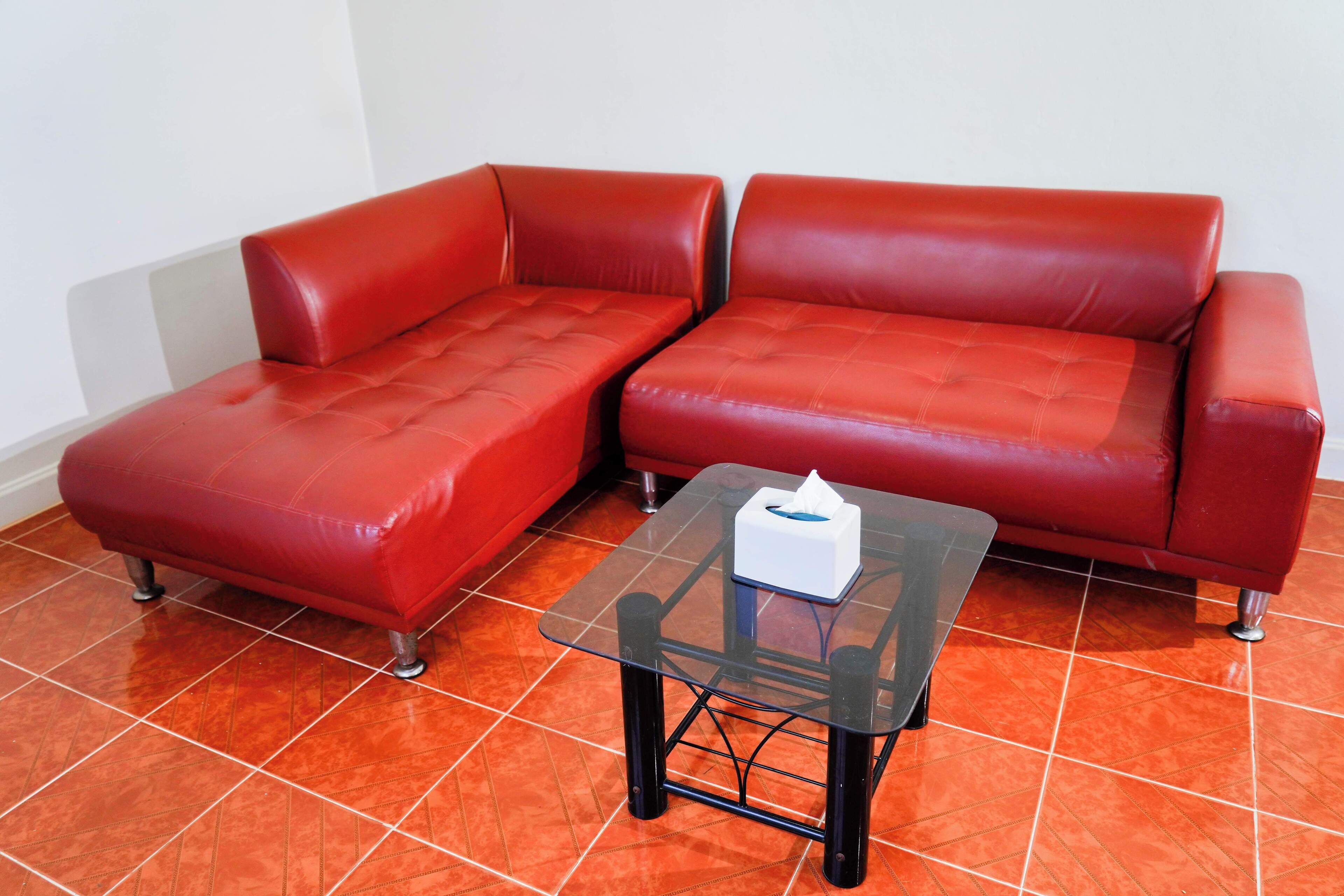 A red leather sofa with a glass coffee table in a room with orange tiled flooring.