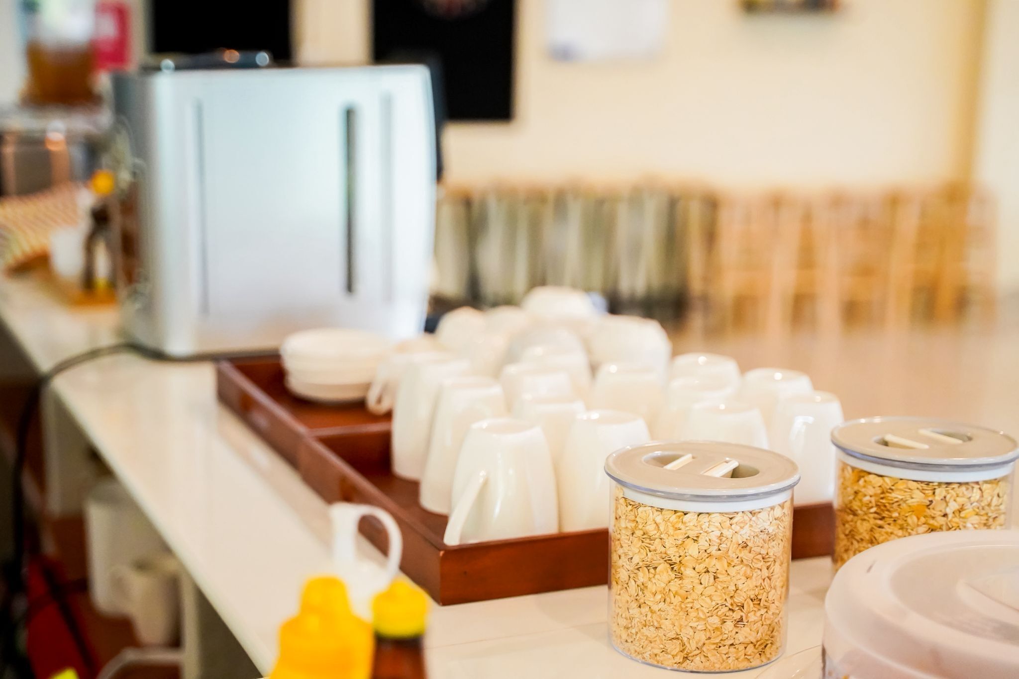 Una barra de desayuno con tazas blancas, un tostador y recipientes con avena y otros cereales.