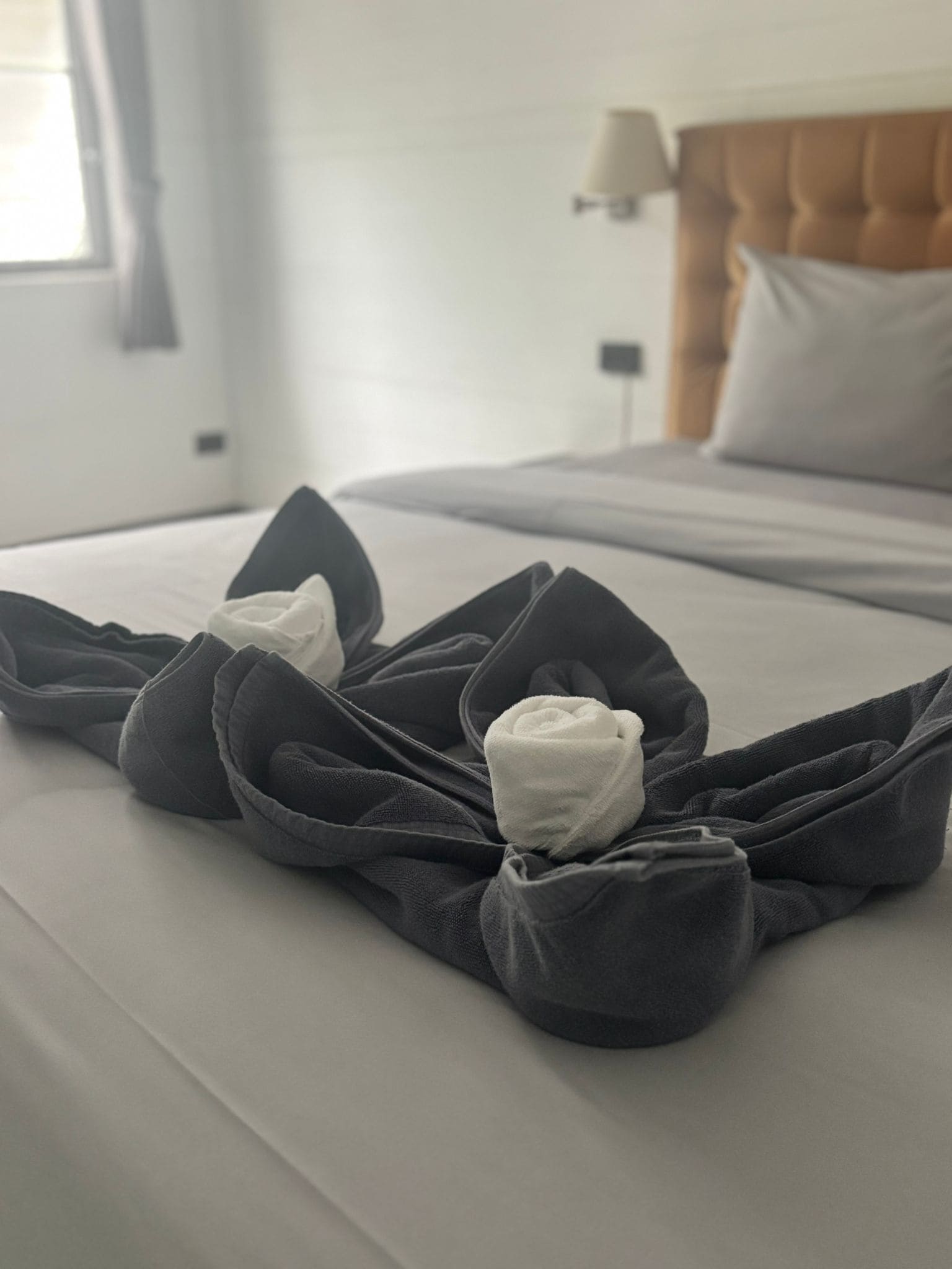 Een opgemaakt bed met een grijze deken en twee opgerolde handdoeken erop.