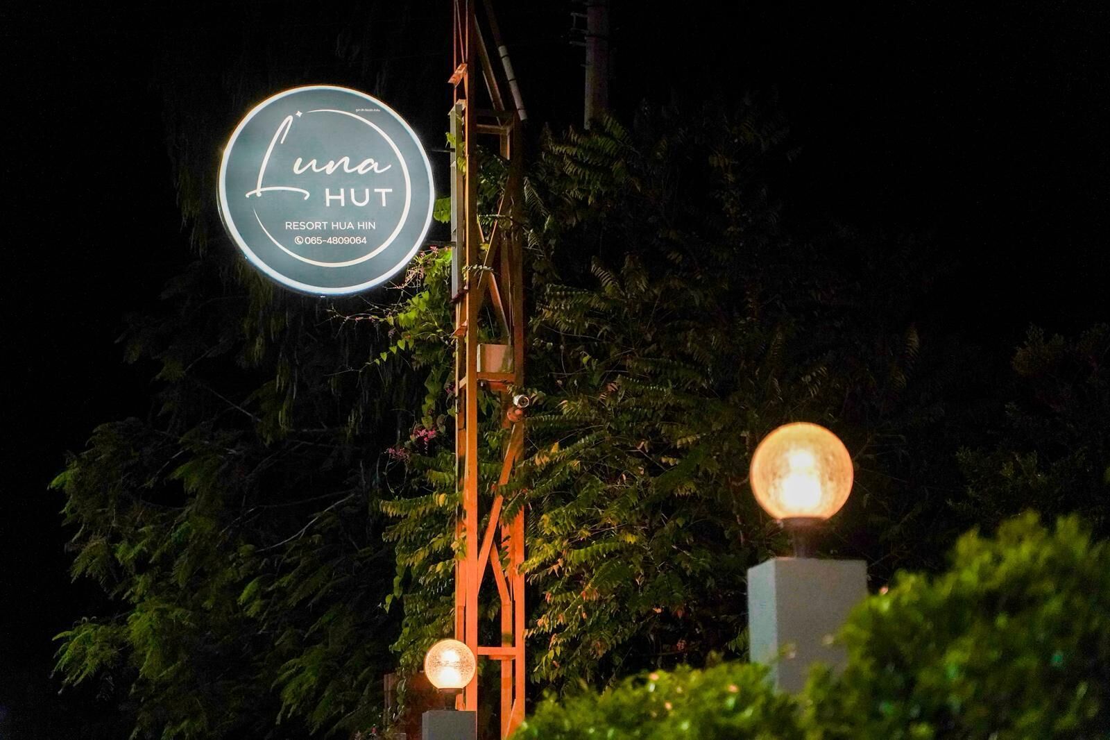 Señal de Luna Hut con un número de contacto, sobre un fondo de follaje y una estructura de madera.