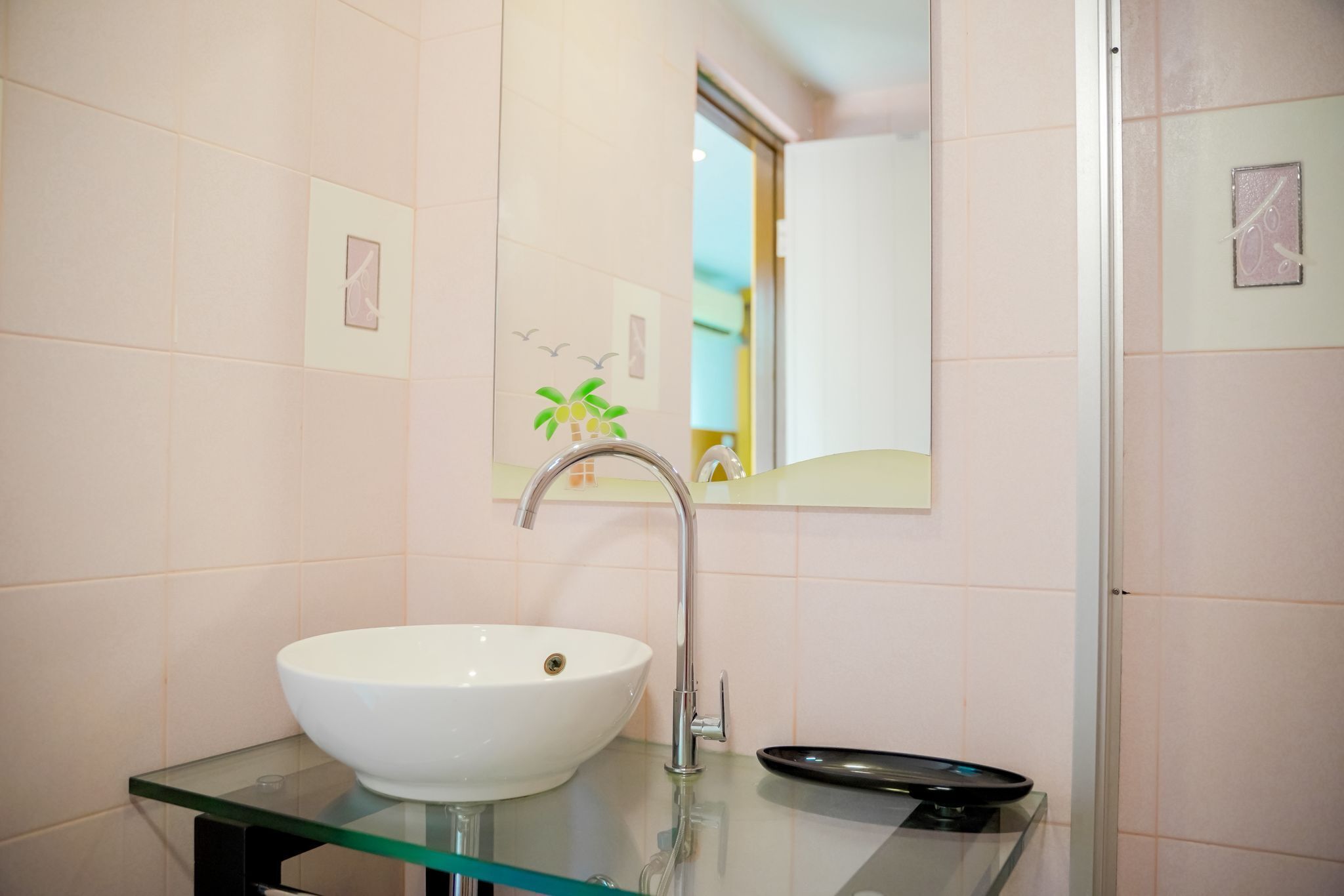 A bathroom with a white sink, a glass countertop, a mirror, and a shower area.
