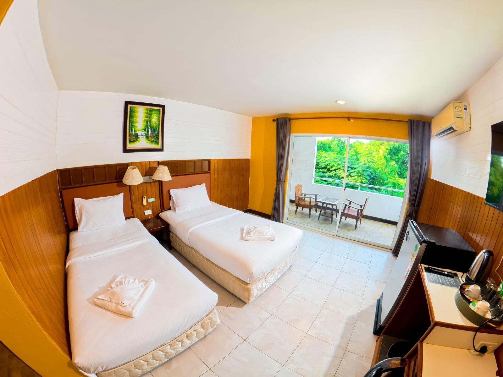 A hotel room with two beds, a desk, a chair, a TV, and a balcony with a view of greenery.