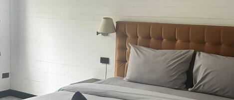Hotelkamer met een bed, hoofdeinde, een aan de muur bevestigde airconditioning, een schilderij van een zonsondergang boven de oceaan, en een lamp.