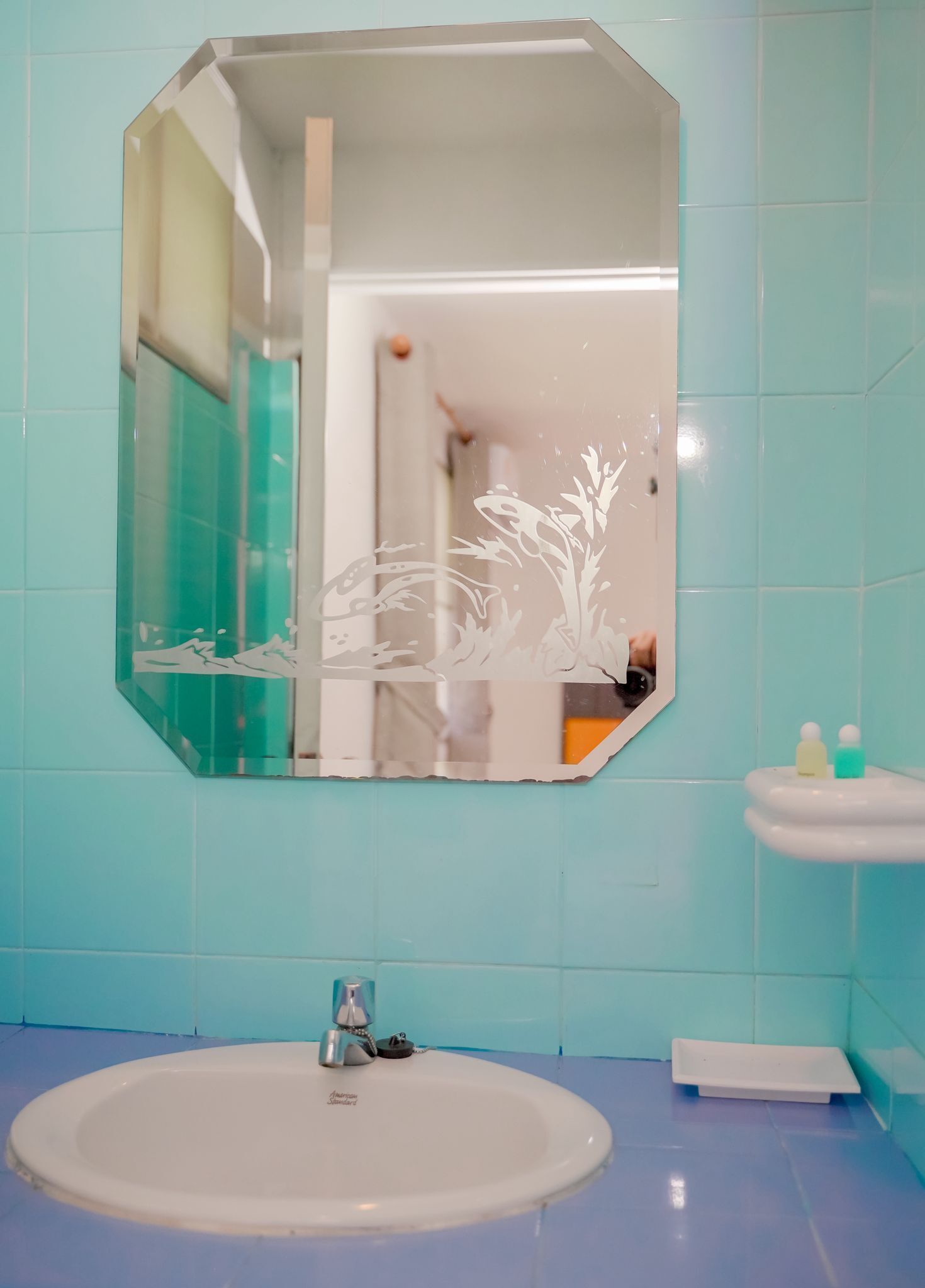 Une salle de bain avec un lavabo blanc, un miroir orné d’un motif floral et un mur recouvert de carreaux bleus.