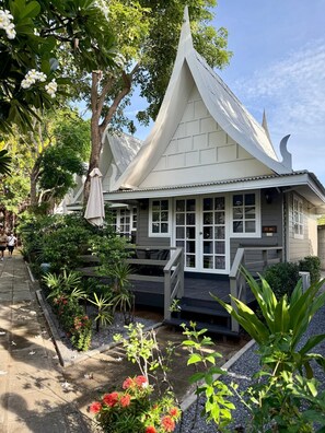 A traditional-style building with a sloped roof, a porch with steps, and a garden with various plants and flowers. - Luna Hut Resort Hua Hin (Hua Hin)