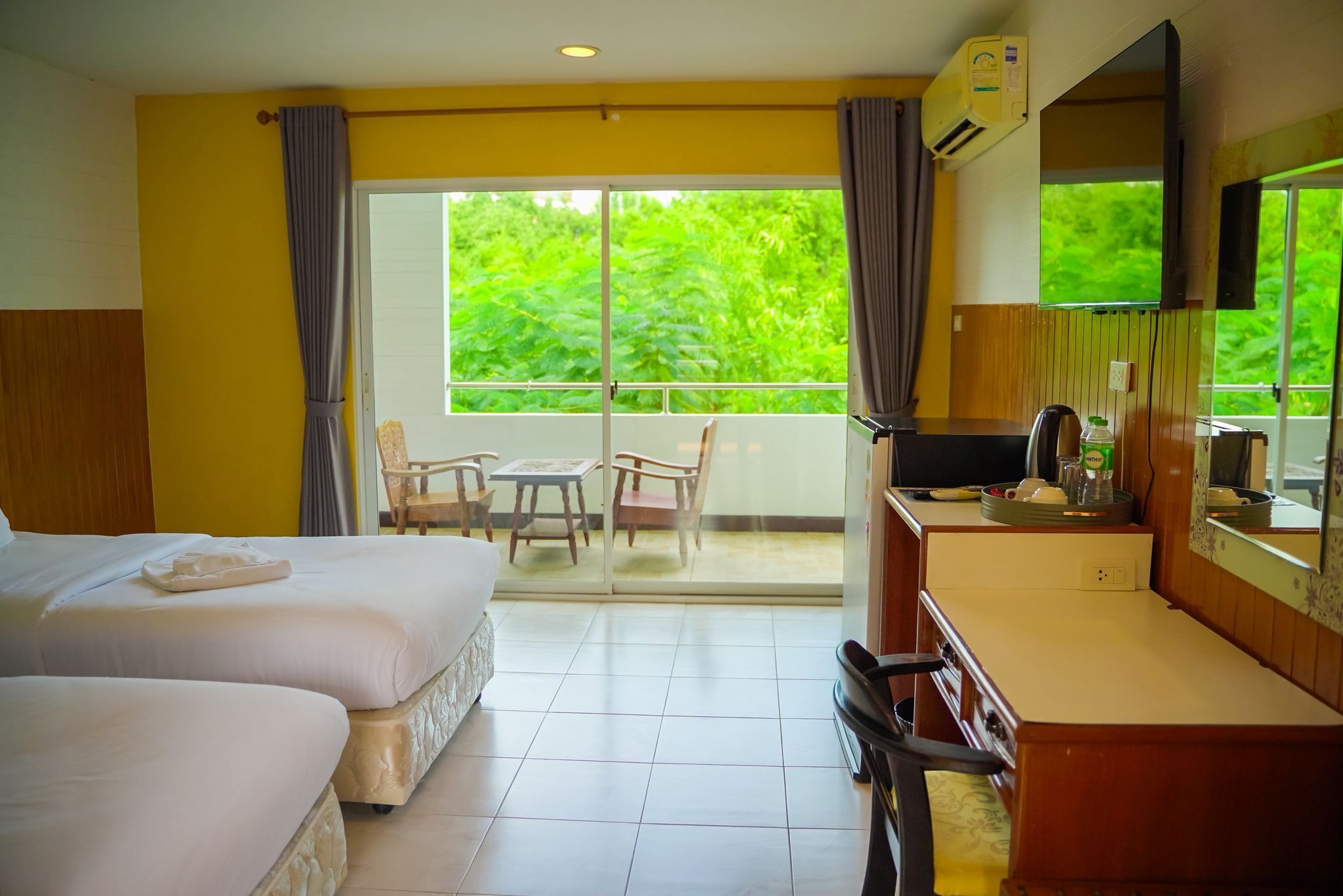 Hotelkamer met twee bedden, een kitchenette, een televisie en een balkon met uitzicht op groen.