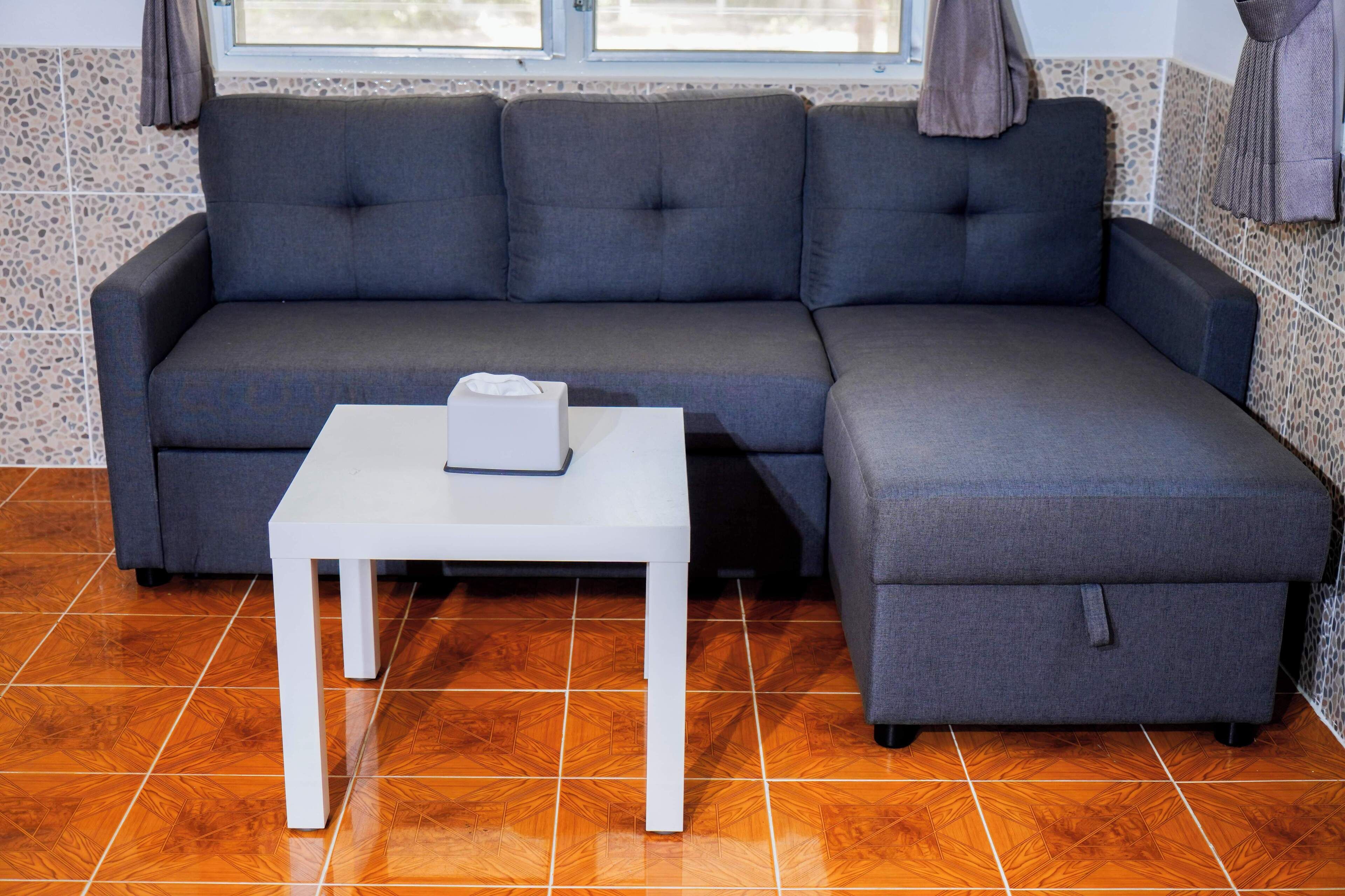 Un canapé gris, une table blanche devant, une fenêtre avec des rideaux et un mur à motifs.