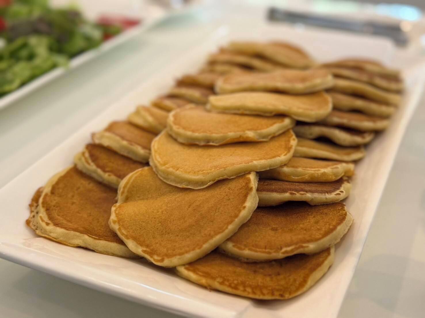 A white rectangular plate with several golden-brown pancakes stacked on top of each other.