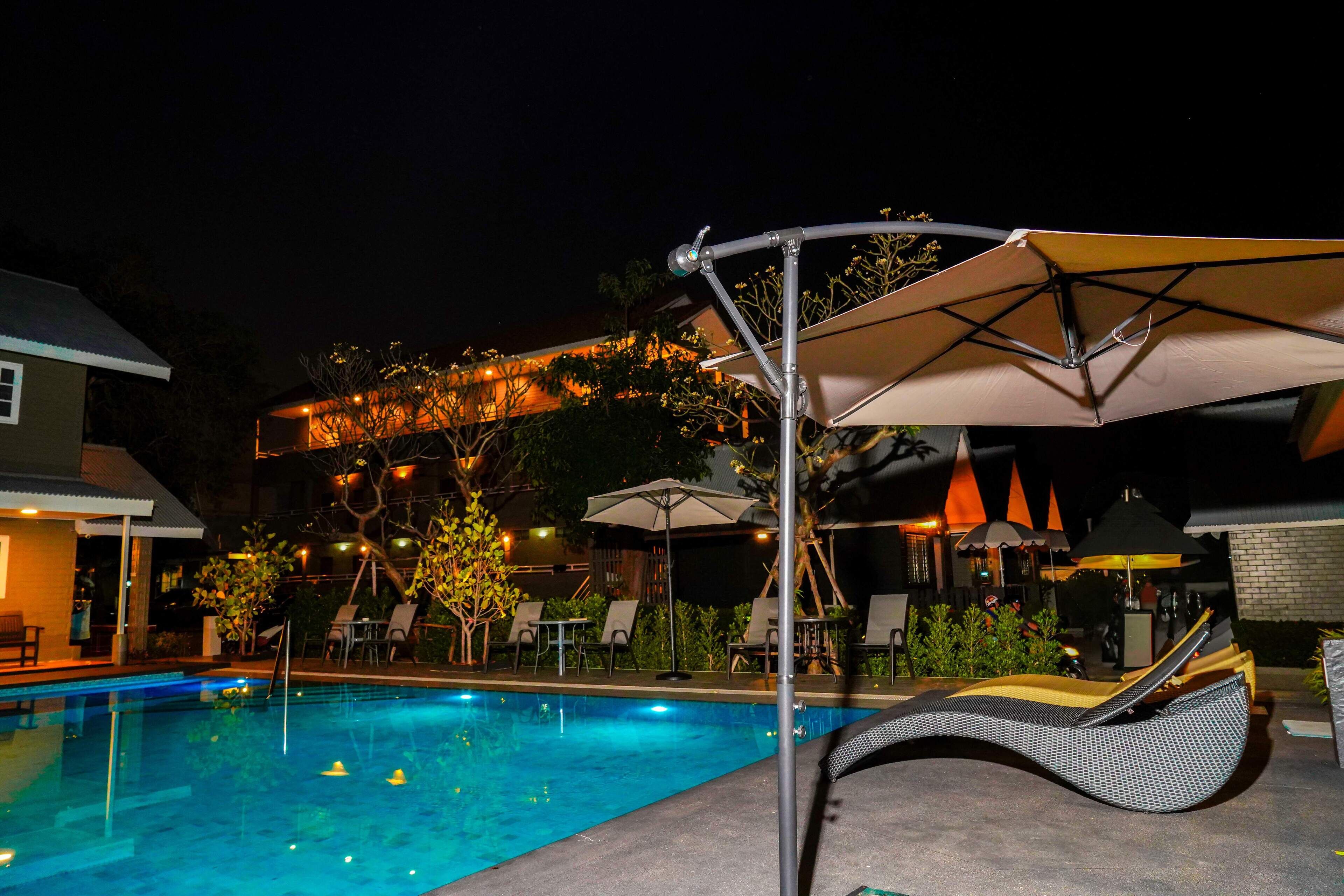 Una piscina con sillones de descanso y sombrillas, rodeada de asientos al aire libre y un edificio con luces.