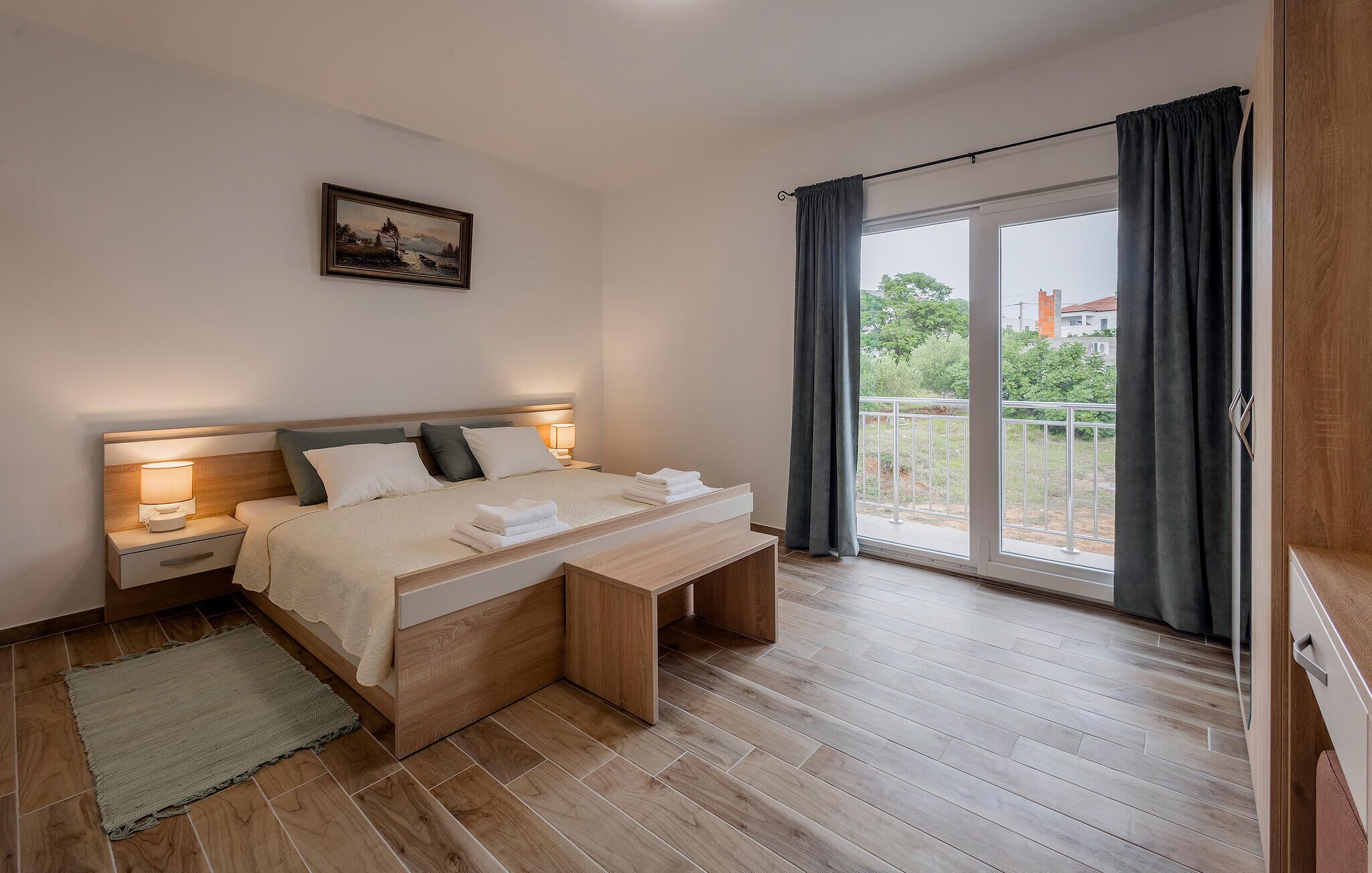 Un dormitorio moderno con cama, mesitas de noche, un banco y vistas al exterior.