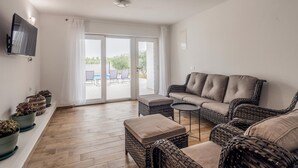 Una sala de estar con un sofá, dos sillones, una mesita y un televisor montado en la pared.