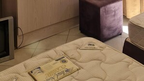 A room with a large wardrobe, a television on top, a purple ottoman, and a bed with a quilt.