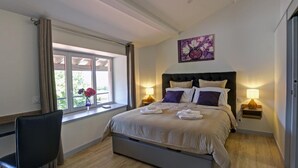 Een slaapkamer met een bed, nachtlampjes, een stoel, een raam met gordijnen en een schilderij aan de muur.