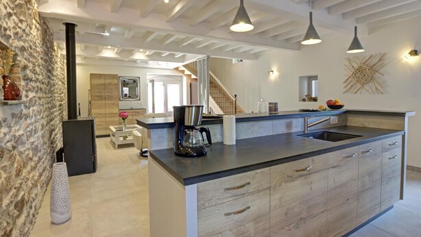 Een moderne keuken met een groot eiland, hanglampen en een accentmuur van steen.