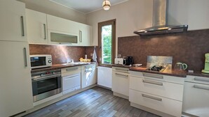 Una cocina moderna con armarios blancos, microondas integrado, horno, cafetera y ventana con vista a la vegetación.