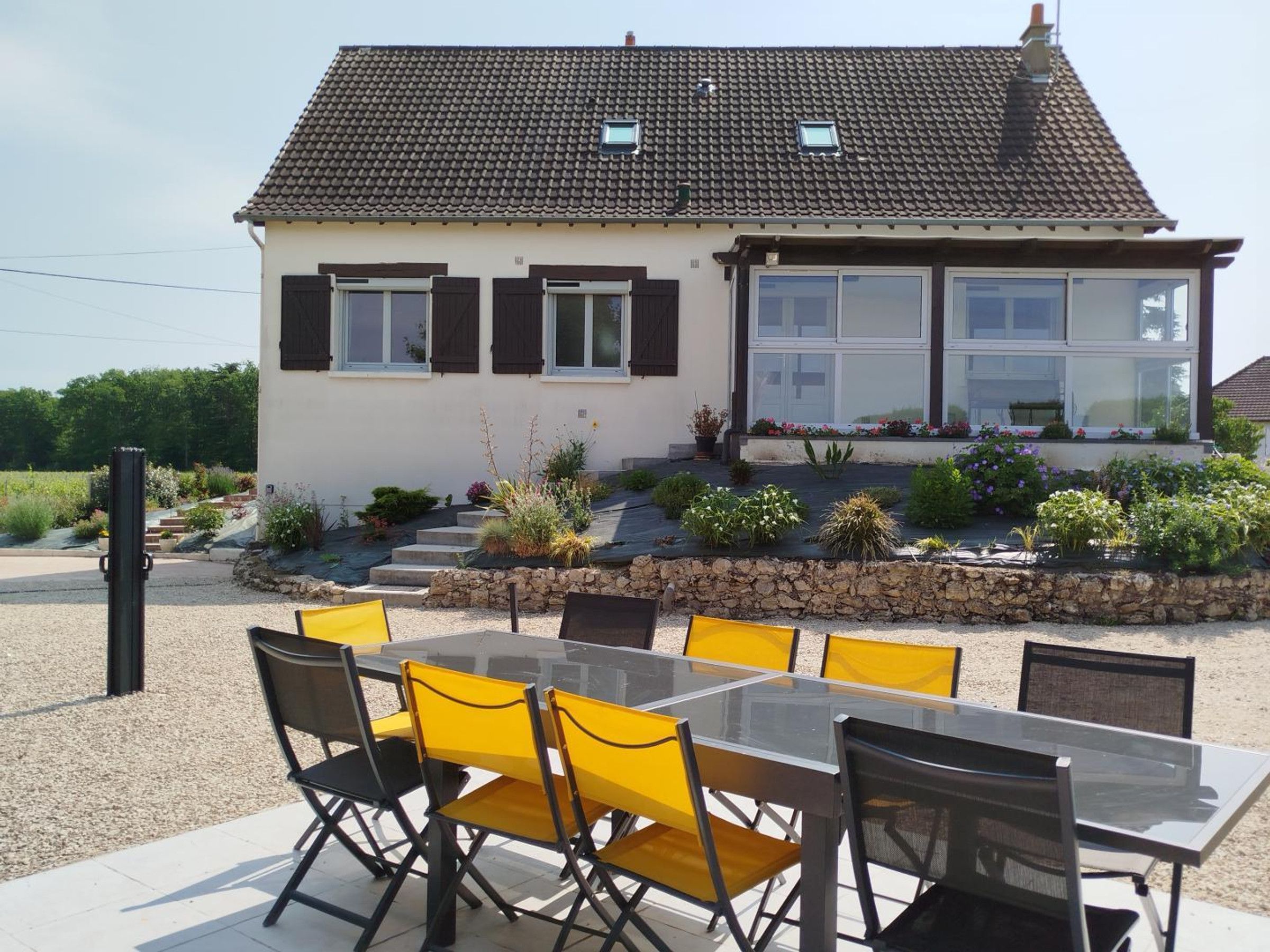 Et toetagers hus med tegltag, en balkon med plantekasser og en terrasse med et glasbord og stole.
