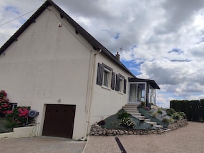 A two-story house with a brown door, a covered porch, and a stone staircase leading to the entrance. - Spacieuse maison près des Châteaux de la Loire avec jardin clos, jeux pour enfants et visites de vignobles (Cheverny)