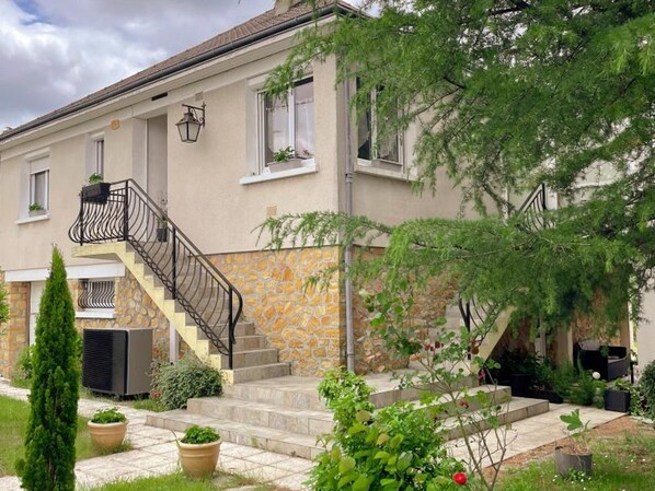 A two-story building with a stone facade, a staircase with a metal railing, and potted plants.