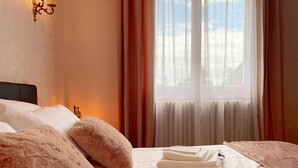 Quarto de hotel com cama, travesseiros macios, mesa de cabeceira com abajur e janela com cortinas.