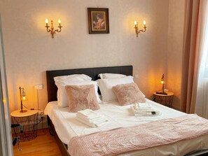 A neatly made bed with white linens and pink accents, two bedside lamps, and a framed picture on the wall.