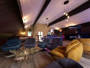 A modern lounge area with comfortable seating, a glass coffee table, and a pool table.