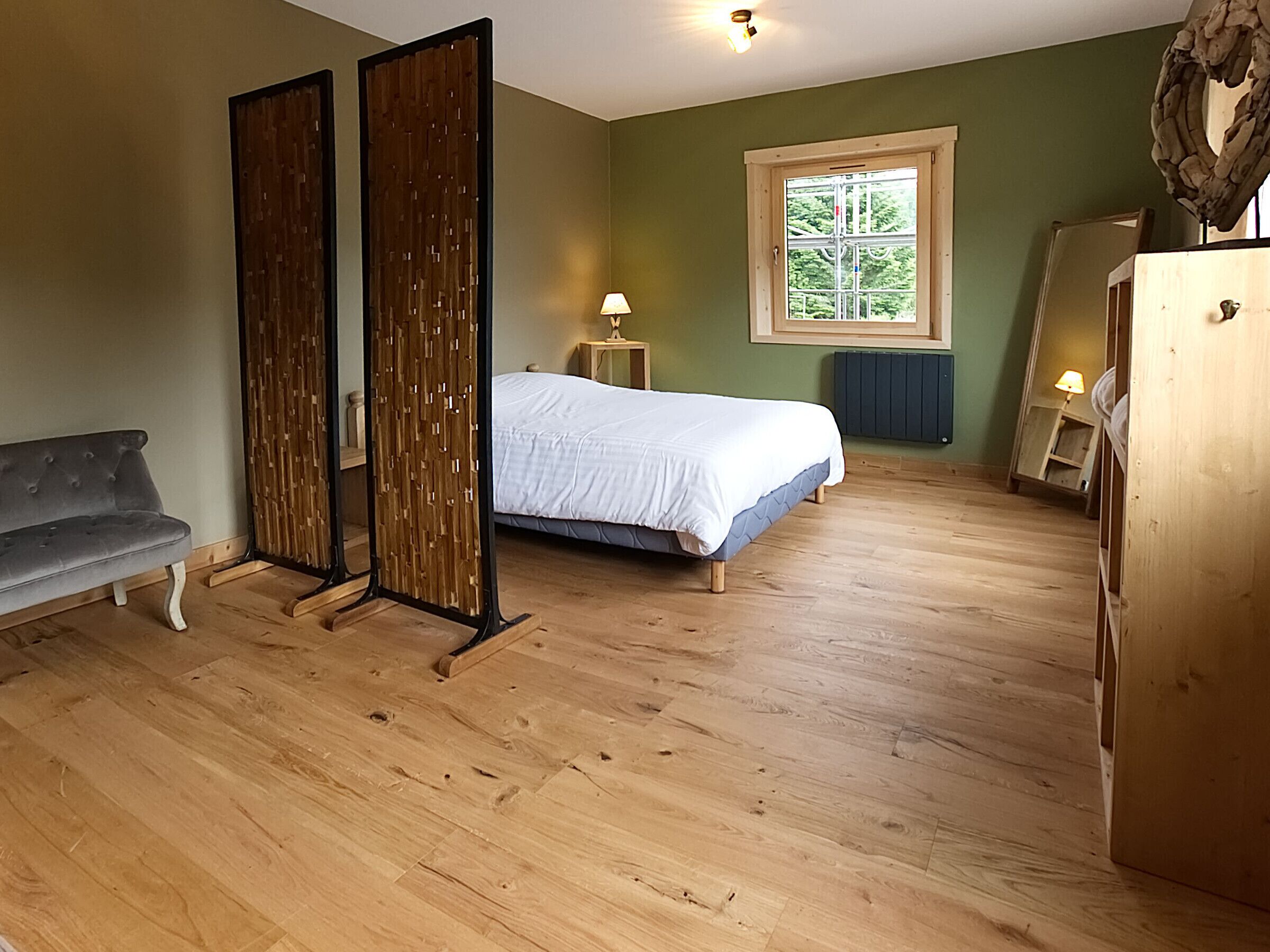 A bedroom with a bed, a bench, a window, and a radiator.