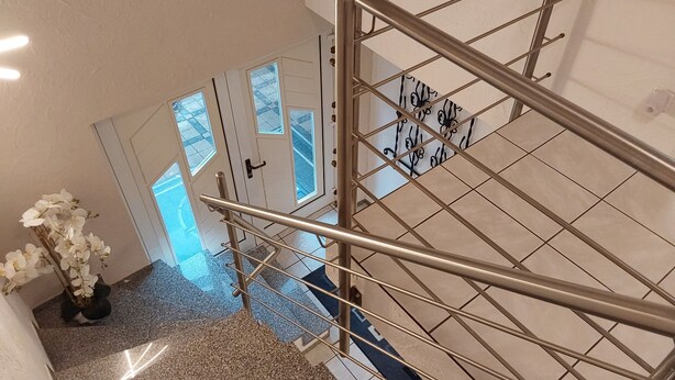 Una escalera con barandilla metálica, una orquídea blanca en maceta y un tapete estampado.