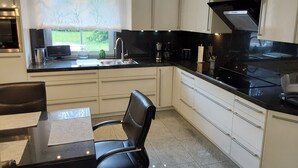Una cocina moderna con armarios blancos, encimera negra y cortina con estampado de árbol.