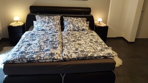 Una cama con colcha estampada con motivos florales, dos mesitas de noche con lámparas y un cuadro de temática forestal.