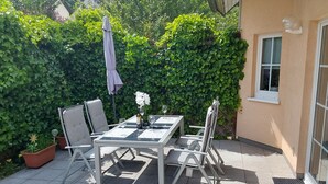 Un patio exterior con una mesa y sillas, rodeado por un seto verde y frondoso.