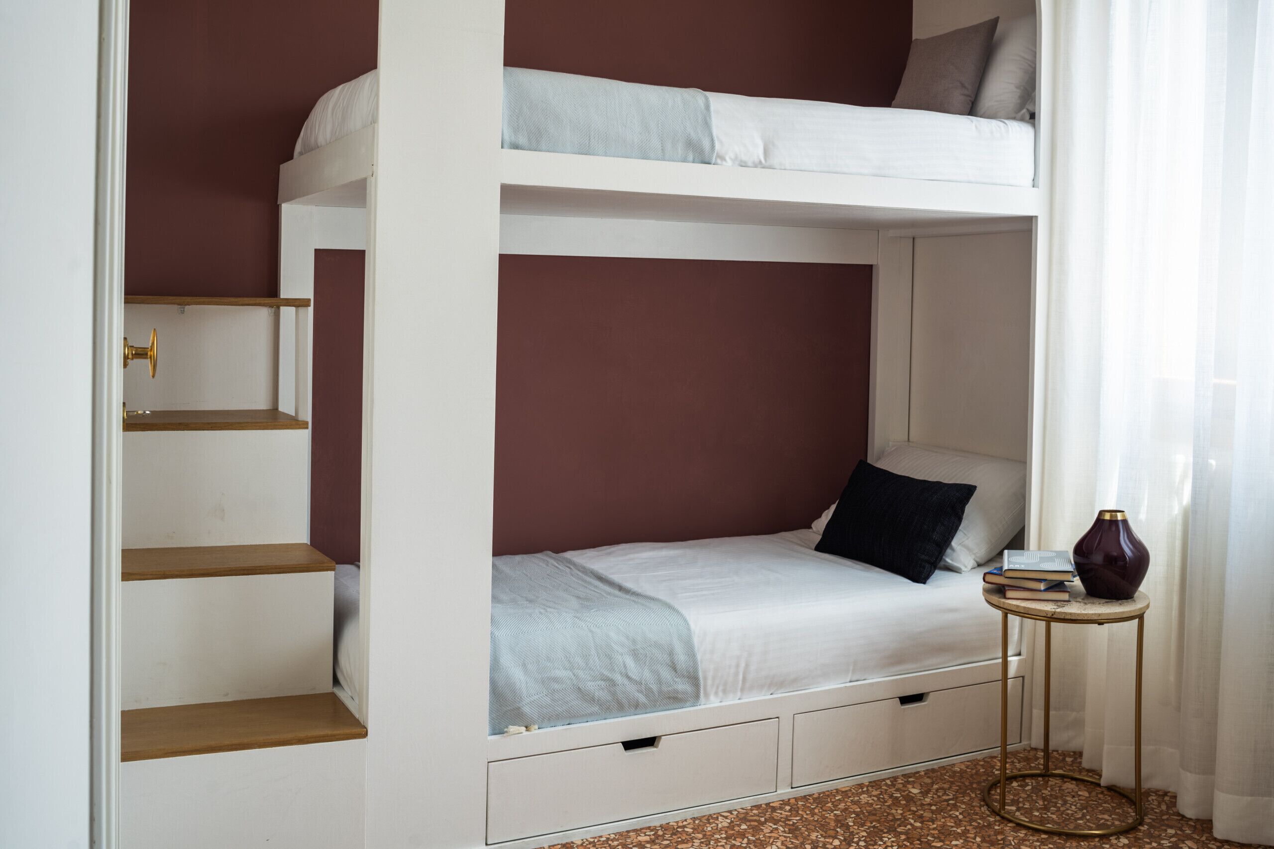 Una cama litera con una cama inferior, una mesita pequeña con libros y un jarrón en el suelo.