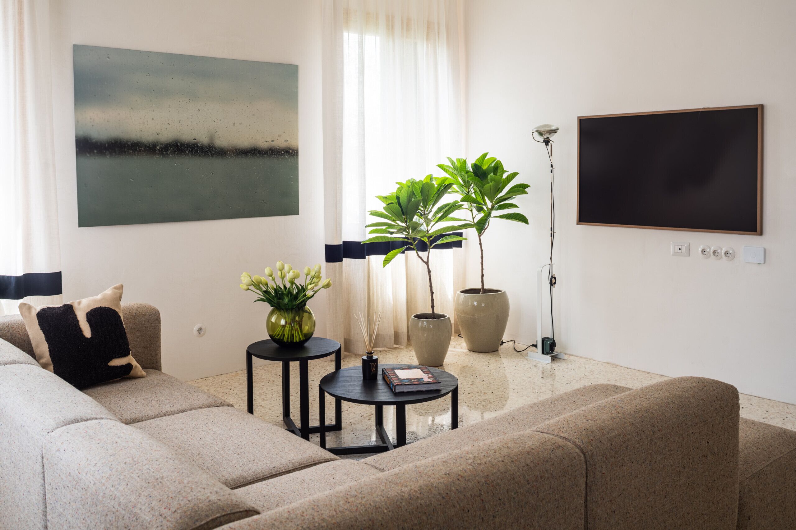 A modern living room with a sofa, two side tables, a floor lamp, and two potted plants.
