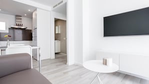 A modern, minimalist living room with a grey sofa, a small white table, and a TV mounted on the wall.