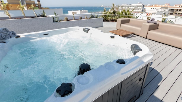 A rooftop deck with a hot tub, outdoor furniture, and a view of the sea.
