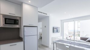 A modern kitchen with a built-in microwave and refrigerator, a dining area with a table and chairs, and a large window offering a view of the city.