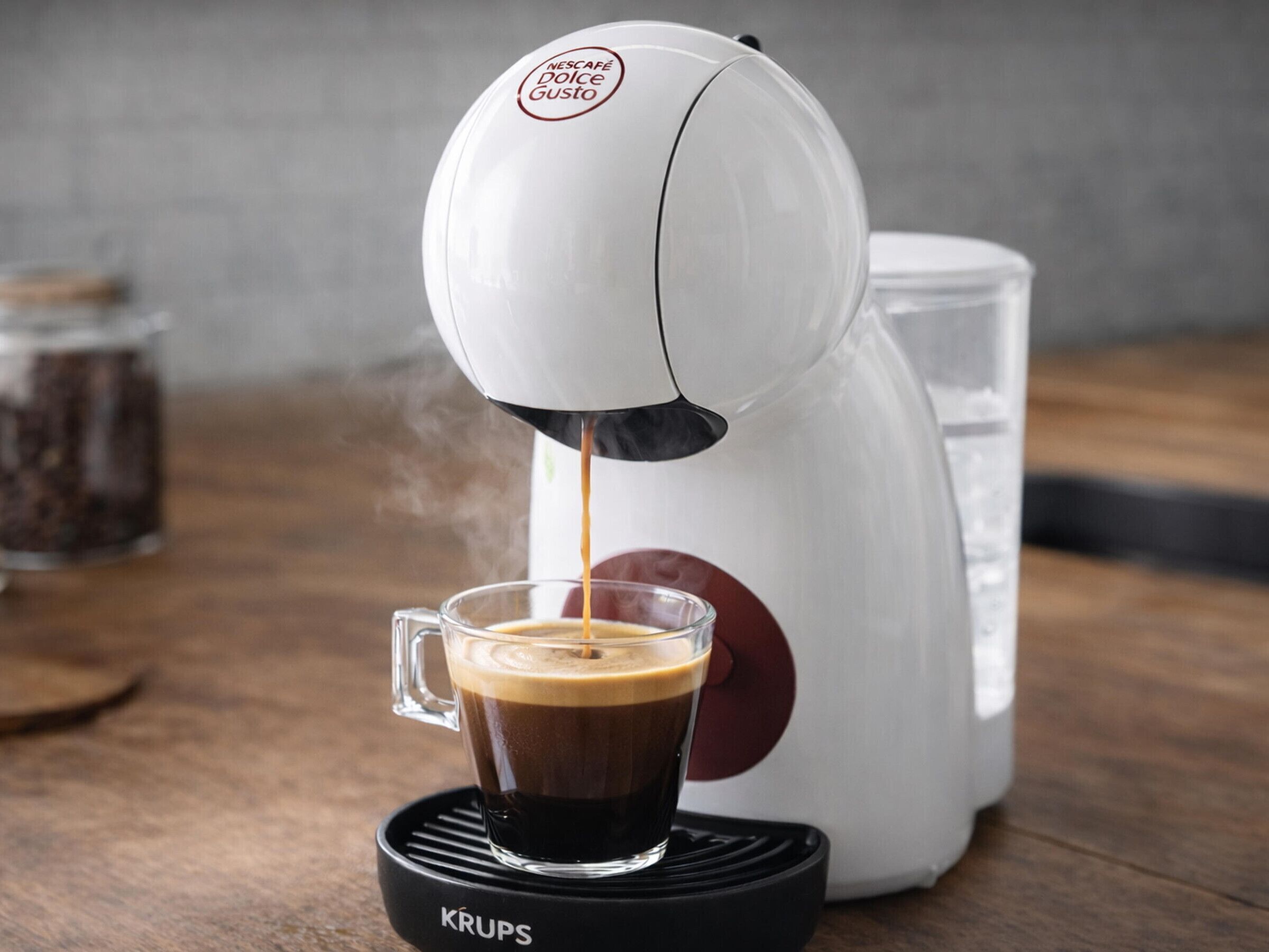 A coffee machine dispensing coffee into a glass cup on a Krups coffee warmer.