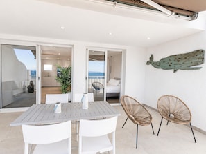 An outdoor dining area with a table and chairs, a potted plant, and a view of the sea.