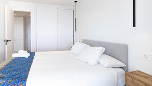 A modern bedroom with a bed, white pillows, a wooden headboard, a ceiling fan, and a patterned area rug.
