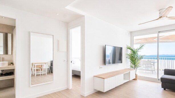 A modern living room with a flat-screen TV, a sofa, a dining area, and a balcony with a view.